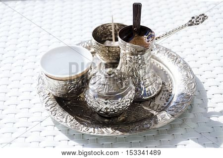 A metallic tray with copper plated cezve (džezva) filled with traditional foam Bosnian coffee a silver pot with turkish delight rahat lokum a clay cup and sugar cube pot served in an ornament Sarajevo set.