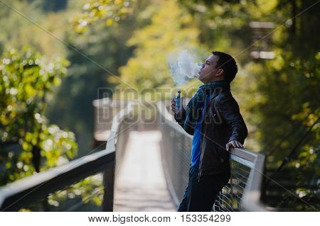 Young man with custom box mode vape device vaping an electronic cigarette outdoor at beautiful place outdoors.