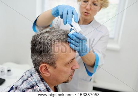 baldness. diagnostics hair and scalp. Trihoskopiya. Doctor examine patient male hair a special apparatus.