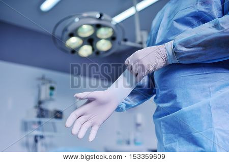 Doctor puts on latex gloves on the background of the surgical lamp. A surgeon preparing for surgery