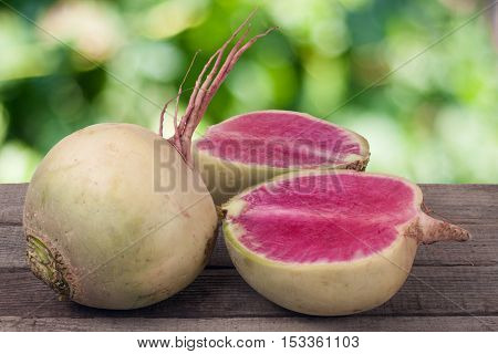 One whole and sliced watermelon radish on a wooden table with blurred garden background.