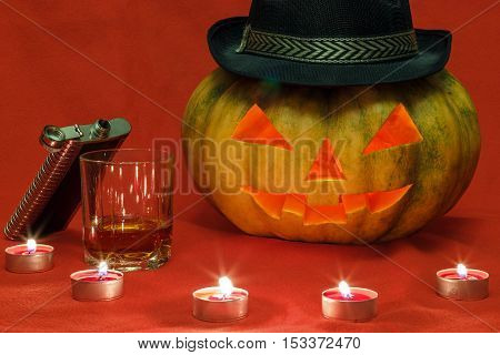 Pumpkin for Halloween with glowing eyes and a glass of whiskey