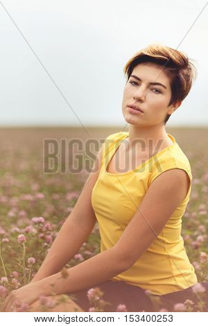 Young caucasian woman with trendy short hair sitting in field among wildflowers. Image with split toned