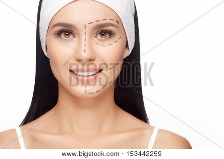 Young woman with perforation lines on her face before plastic surgery operation. Beautician touch and draw correction lines on woman face. Isolated