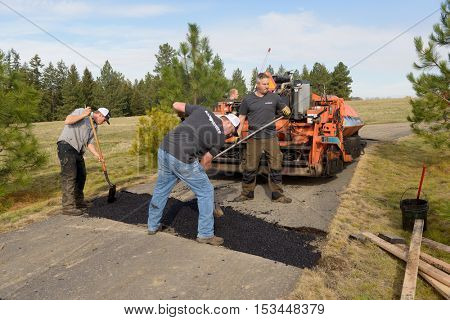 Colbert, WA - October 24, 2016: Workers from Black Diamond Asphalt Paving, LLC., repairing patches and re-paving a private road/driveway