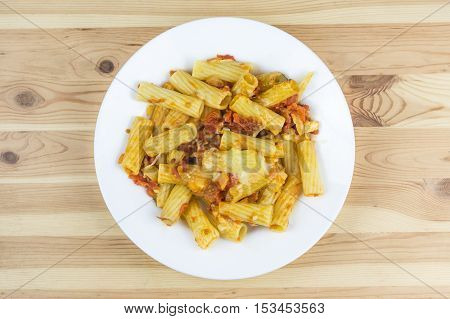 Top view of baked tortiglioni pasta with tomato sauce mozarella and parmesan cheese in the plate on the wood table
