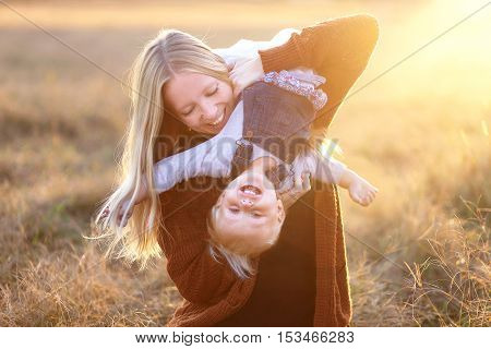 Happy Young Mother Playing With Baby Daughter Outside At Sunset