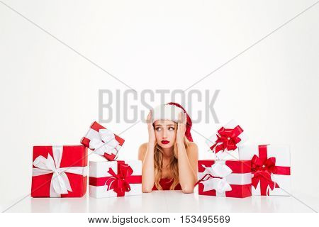 Sad upset young woman in santa claus costume with gift boxes over white background