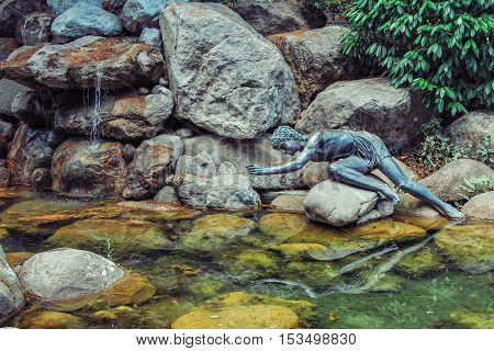 Partenit Village, Crimea/Ukraine - June 07, 2012: Copper sculpture of Narcissus sitting on a rock in a pond, admiring self reflection on a water surface, legend scene reconstruction.