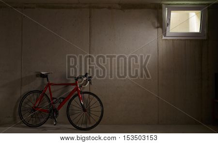 Single red bike leaning on wall in garage with partially open window and copy space on the other side