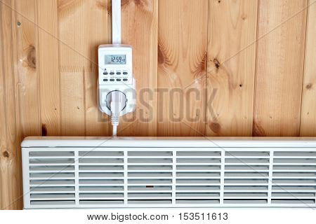 Working white electric convector heater plugged to timer power socket operated in smart house system against wooden wall inside room front view closeup