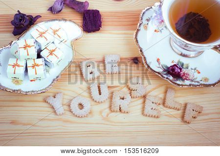 Be Yourself, inspirational slogan made from biscuit letters with chocolate sweets and a cup of tea on wooden background. Toned image.