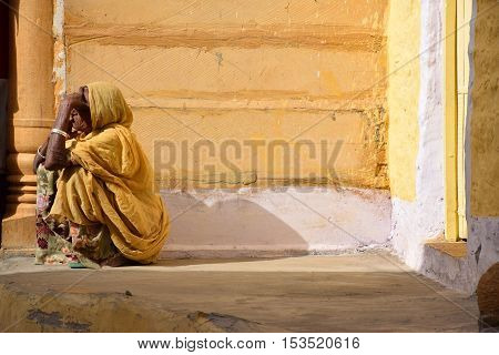 JAISALMER, RAJASTHAN, INDIA - FEBRUARY 10, 2016 - Unidentified aged indian woman sitting outside her house with gold painted walls