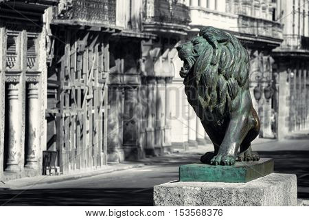 Black and white street scene of Old Havana with the symbolic bronze lion statue at El Prado avenue in its original color