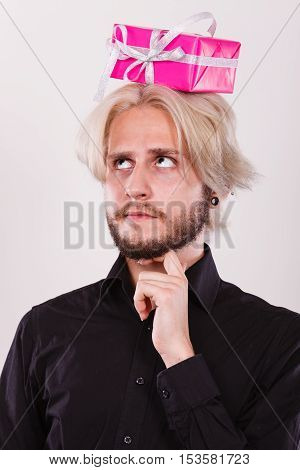 Celebration and giving concept. Cool young man with pink gift box on his head. Guy thinking looking for present idea