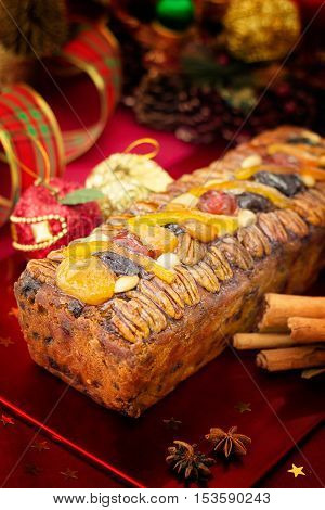 Traditional Christmas fruit cake with festive decorations and Xmas spices on red background.Vertical compositon