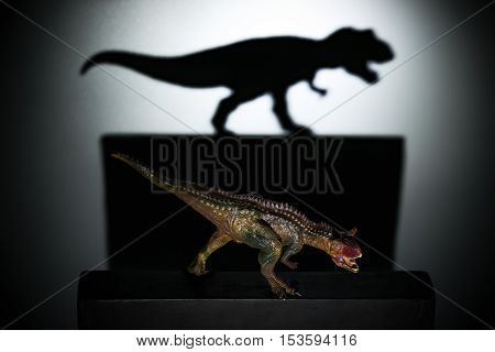 a carnotaurus casting a tyrannosaurus shadow in dark concept of strength and aspirations