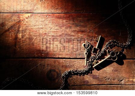 Three vintage keys on old wooden background under beam of light