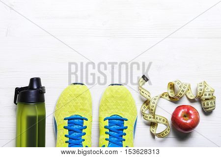 Sports equipment - sneakers, skipping rope, dumbbells, smartphone and headphones. Sport background on wooden floor, top view.