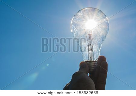 hand hold a light bulb with sunshine power concept white blue sky background