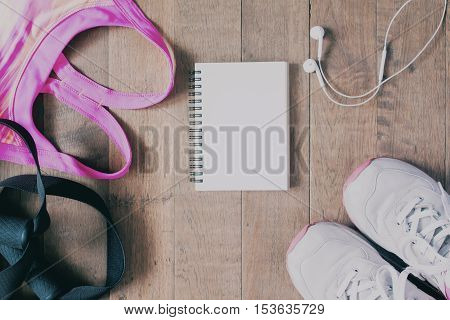 Flat lay of empty notebook pink color sport bra sport equipment earphone and sneaker on wood background. Sport fashion Sport accessories top view copyspace with film color filter