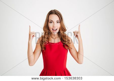 Cheerful beautiful young woman standing and pointing up over white background