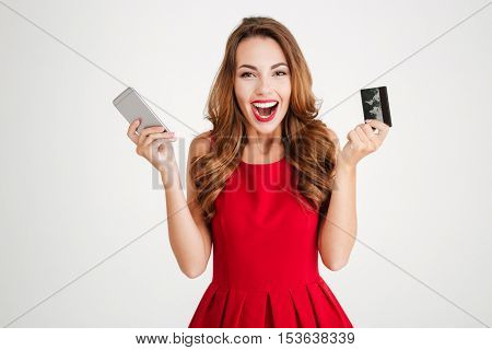 Cheerful excited young woman with mobile phone and credit card over white background