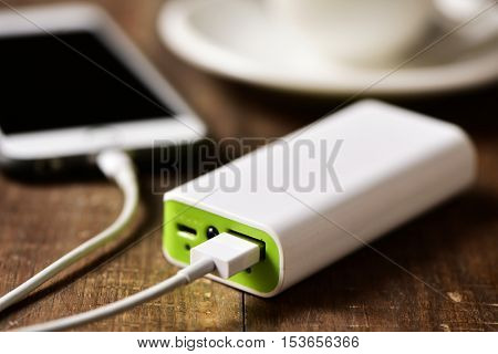 closeup of a powerbank charging a smartphone placed on a wooden table next to a cup of coffee