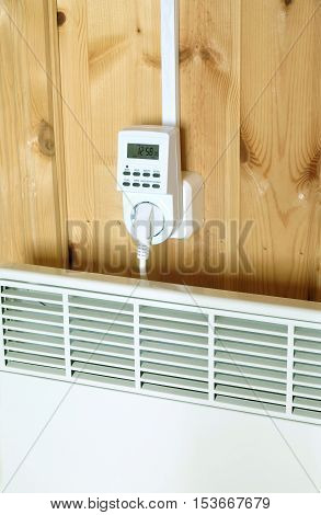 Working white electric convector heater plugged to timer power socket operated in smart house system against wooden wall inside room side view closeup