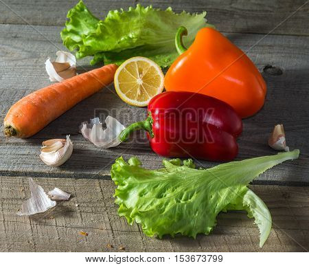 Still life with salad leaves lemon carrots yellow and red peppers garlic on an old wooden table front view.