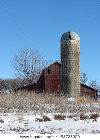 An old abandoned barn and Silo against a clear blue sky.