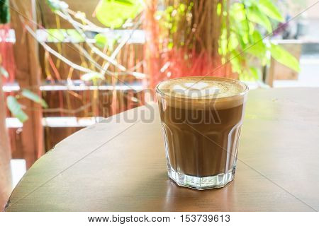 Hot latte in glass with heart shaped latte art on wooden table