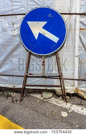 Old mandatory direction sign with scratches and dents in construction site.