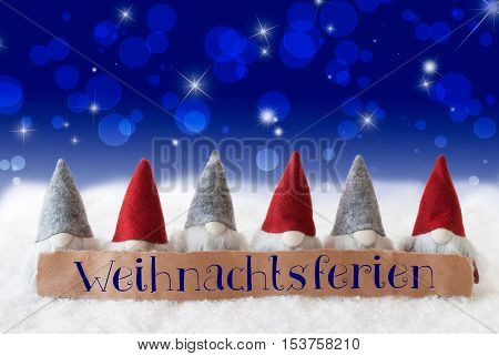 Label With German Text Weihnachtsferien Means Christmas Break. Christmas Greeting Card With Gnomes. Sparkling Bokeh And Blue Background With Snow And Stars.