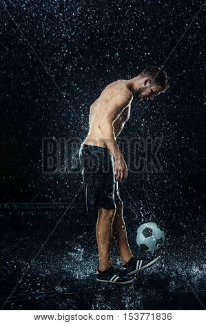 Water drops around football player on black background
