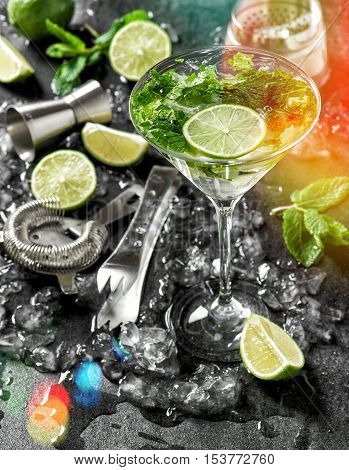 Cocktail drink with lime mint and ice. Disco bar tolls and ingredients on dark background with light leaks