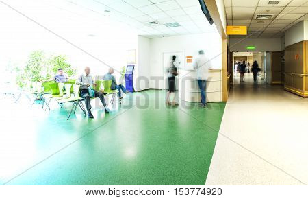 View of the registration desk, waiting area and a corridor in modern hospital with blurred figures of patients and a copy space.