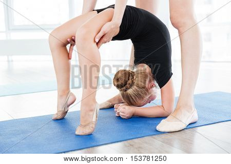 Young ballerina girl doing stretching exercises with her female teacher at sudio