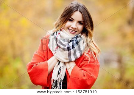 Beautiful young happy girl in red coat autumn scarf wrapped in a warm autumn day
