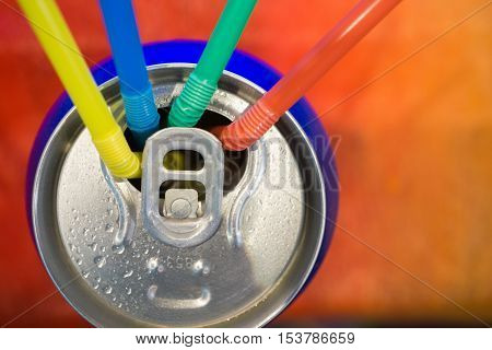 four different drinking straws in an open soda beer wet can. Top view over colored contrast background. closeup macro image