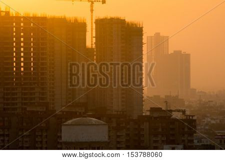 Under construction buildings shot during the golden hour in Noida Delhi India. The crane on top of the multi storey skyscraper is clearly visible
