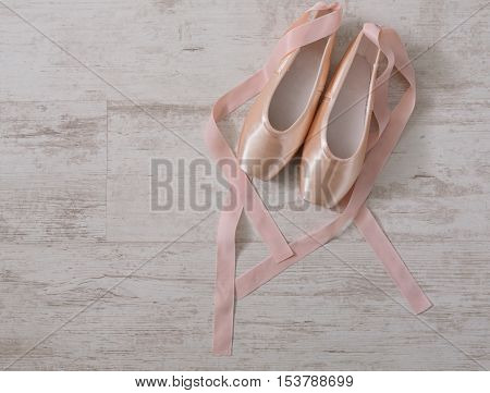 Pastel pink ballet shoes background. New pointe shoes with satin ribbon lay on white rustic shubby chic wood, top view with copy space