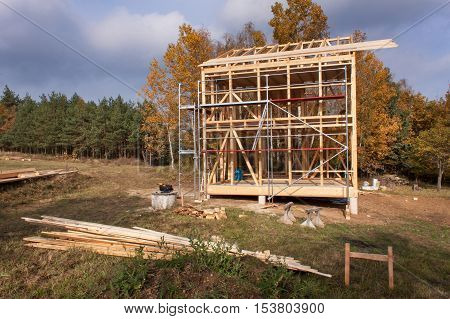 Metal scaffolding around the unfinished house. Construction of ecological house. Wooden frame of house under construction.Framed New Construction of a House. Timber house in building process