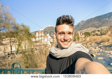 Young handsome man taking selfie by Passer river at Meran old town in South Tyrol in Italy - Adventure and travel lifestyle concept - Composition with tilted horizon and warm afternoon color tones