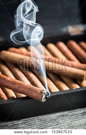 Burning Cigar On Wooden Humidor Full With Cigars