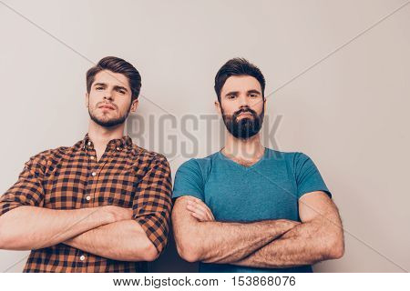Two handsome serious men with crossed hands isolated on gray background