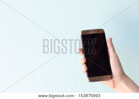 Bangkok Thailand September 10 2016 : Woman held android phone Samsung galaxy S7 Edge on blue concrete background. Samsung S7 Edge is smart phone with multi touch screen