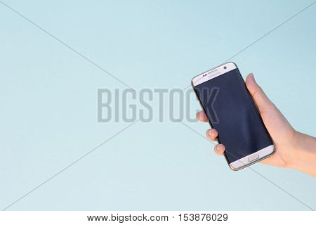 Bangkok Thailand September 10 2016 : Woman held android phone Samsung galaxy S7 Edge on blue concrete background. Samsung S7 Edge is smart phone with multi touch screen