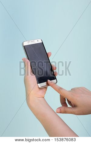 Bangkok Thailand September 10 2016 : Woman held android phone Samsung galaxy S7 Edge on blue concrete background. Samsung S7 Edge is smart phone with multi touch screen