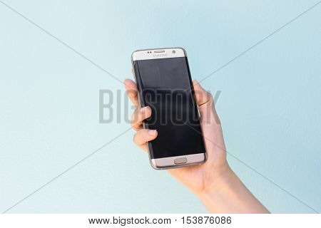 Bangkok Thailand September 10 2016 : Woman held android phone Samsung galaxy S7 Edge on blue concrete background. Samsung S7 Edge is smart phone with multi touch screen